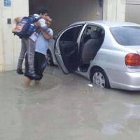 اب يحمل ابنه تجنبا لمياة الامطار